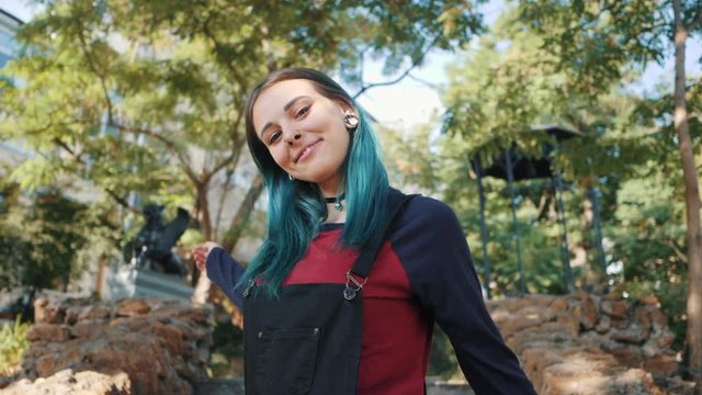 Street punk or hipster girl enjoying empty old European park. Portrait of teen girl with blue dyed hair,piercing in nose,violet lenses and unusual hairstyle dancing.Carefree concept. Slow motion.