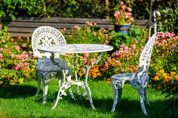 White metal outdoor furniture group in garden. One table and two chairs in vintage style with autumn flowers in background. - 171426259