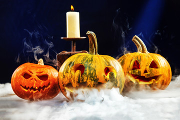 Halloween wallpaper with three jack-o-lantern pumpkins surrounded by smoke at blue background.