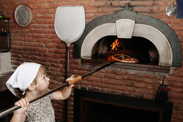 Baby baker takes out pizza from the wood-burning stove