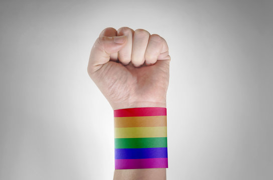 Close up of a young caucasian man with his fist raised and a paper band patterned as the rainbow flag