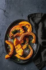 Roasted sliced pumpkin with balsamic sauce, greens and sea salt. Served on vintage metal tray with textile napkin over black texture background. Top view with space