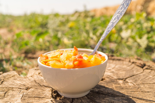 Stew from aubergines, tomatoes, onions, carrots and peppers with tablespoon on the wooden stump in the garden