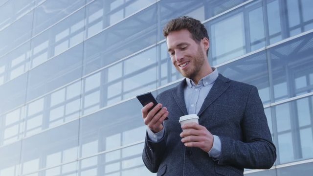 Business man drinking coffee using mobile cell phone app in city to play video games or text sms online. Young urban professional businessman enjoying coffee break relaxing using smartphone.