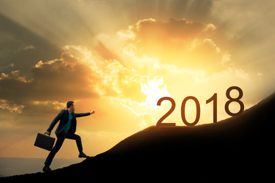 Silhouette of successful businessman with briefcase walking to top of mountain with powerful of sunlight sky background. Young worker reaching goal of 2018, success and achievement concept.Copy space.