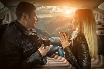 Couple in car. Blonde female and male drink tea in trunk in them