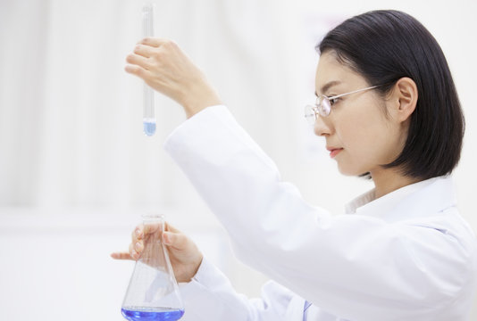 Side view of female scientist looking at flask and test tube