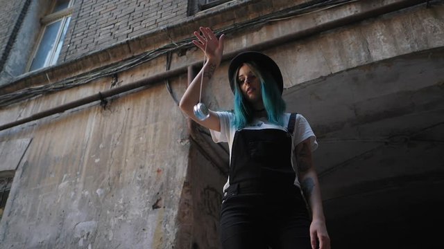 SLOW MOTION: emo girl playing with old school toy yo yo. Street punk or hipster with blue dyed hair,piercing,lenses,tattooed,ears tunnels and unusual hairstyle stands in backyard.