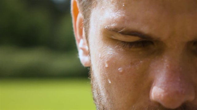 Epic extreme close-up shot of sweaty man outdoor in park. Drop of water on his face macro slow motion. Turning head from dowm to camera