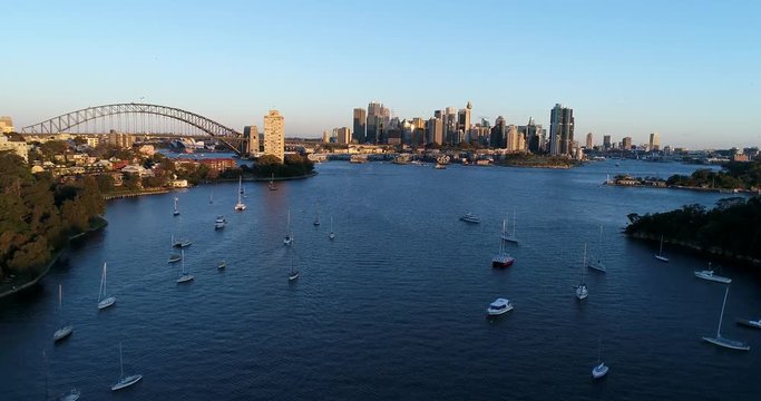Aerial drone view of Sydney City CBD, harbour bridge and harbour above Berry bay at sunset. Docked private yachts in Balls Head reserve and  high-rise towers of Sydney with Ferry.