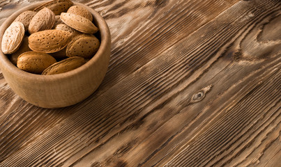 Raw almond in shells in wooden bowl on rustic table background