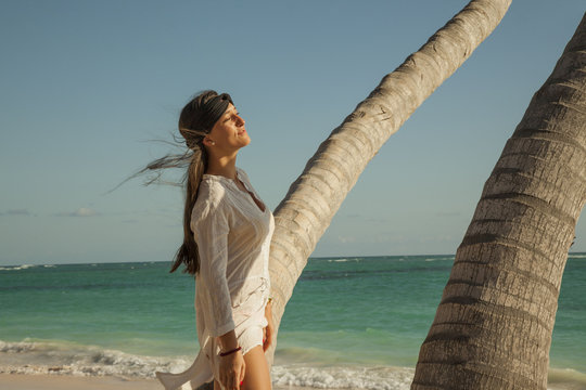 Woman wearing white blouse sunbathe near a palm tree. Tropical caribbean beach.