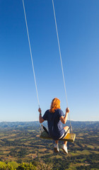 Fototapeta na wymiar Red haired teenage girl swinging on a swing