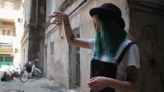 SLOW MOTION: emo girl playing with old school toy yo yo. Street punk or hipster with blue dyed hair,piercing,lenses,tattooed,ears tunnels and unusual hairstyle stands in backyard.