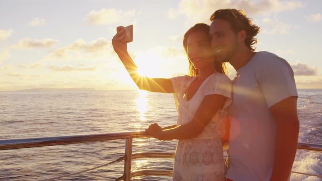 Cruise ship - Romantic couple taking selfie at sunset over the ocean on small cruise ship sailing on open sea. Woman and man taking cell phone photos on boat travel sailing during vacation.