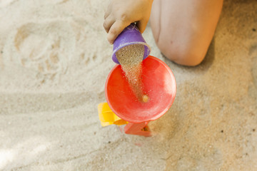 Hands throwing sand in a plastic mill toy in a sandbox. Movement. High angle