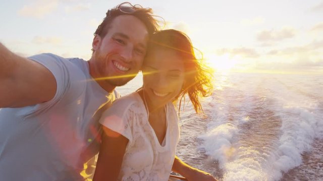 Selfie video - Romantic couple taking selfie video by sunset over the ocean on small cruise ship sailing on open sea. Woman and man taking cell phone photos on boat travel sailing during vacation.