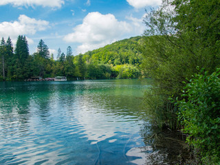 Parco Nazionale dei Laghi di Plitvice. Una collina alberata che domina l'acqua del lago con un fantastico cielo con nuvole sullo sfondo e con un traghetto in lontananza. © mass911