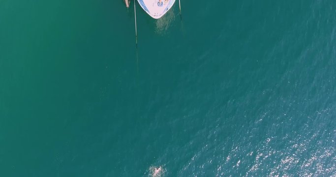 Daytime aerial view of person swimming towards large yacht or fishing vessel in open sea. Travel and recreation concept, panning effect