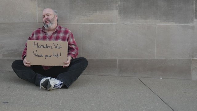 Homeless man on a winter's day holding a sign and sitting on the sidewalk.