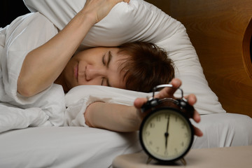 Young woman turning off the alarm clock on the bed