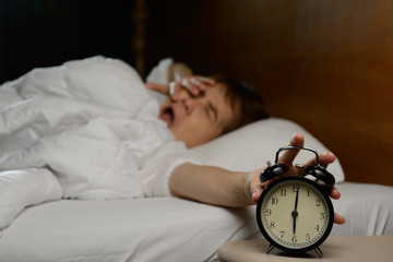 Young woman turning off the alarm clock on the bed