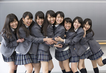 Portrait of cheerful high school girls standing side by side in front of blackboard