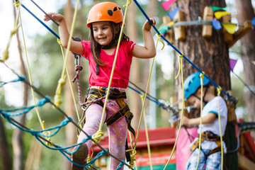 Little beautiful girl climbs on rope harness in summer city park.