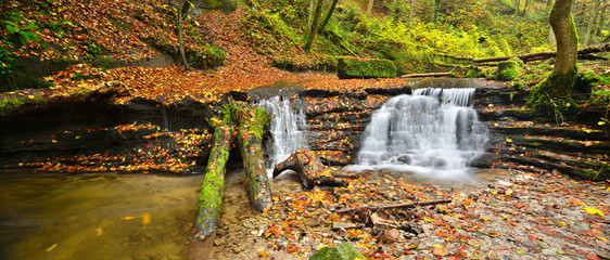 Small Waterfall Covered by Colourful Leaves in Autumn Forest