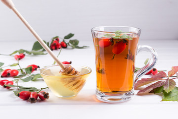 Rose hip tea in transparent cup with honey and fresh berries. Vitamin C drink on white  background.