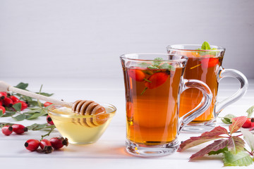 Rose hip tea in transparent cup with honey and fresh berries. Vitamin C drink on white  background.