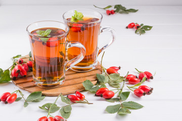 Rose hip tea in transparent cup with honey and fresh berries. Vitamin C drink on white background.