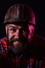 Worker with brutal image wears dirty red helmet and shirt