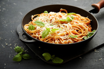 Pasta with tomato and basil in frying pan on black shabby background 
