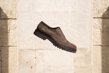 Men's brown suede brogues shoes with black sole on a white background of sand stone blocks. Fashion...
