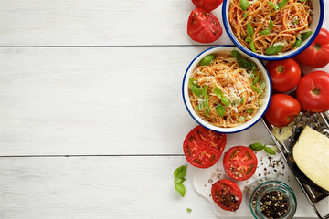 Pasta with tomato and basil in bowls on white wooden background 
