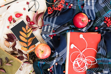 Hot coffee in mug with plaid or scarf, mobile phone with headphones, autumn leaf on a vintage table surface, selective focus