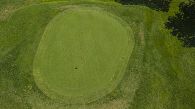 Vista aerea di un campo da golf. Nel dettaglio si vede il prato della buca finale e la bandiera rossa di segnalazione. Il sole splende ed è una giornata ideale per fare sport e stare alla aria aperta.