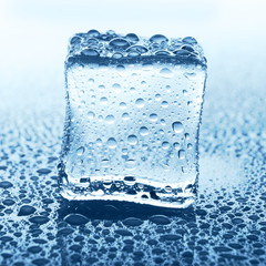 Transparent ice cube on blue glass with water drop