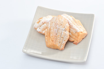 Freshly baked Madeleine cookies sprinkled with sugar powder close-up on the table, petite madeleine isolated on white background.