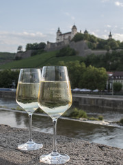 pair of white wine glasses on stone wall with landscape in the background of a Wurzburg wine estate and its vineyards in the northern Bavaria region, Germany.