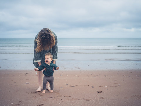 Mother helping baby walk on the beach