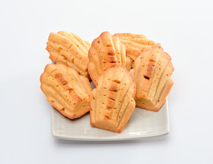 Freshly baked Madeleine cookies sprinkled with sugar powder close-up on the table, petite madeleine isolated on white background.