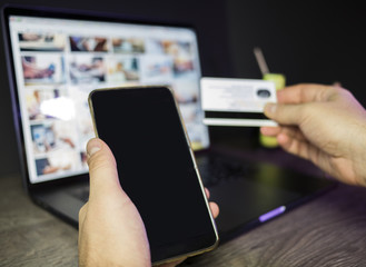 Laptop and credit card in man's hand on dark wooden table surface, selective focus. Business and finance concept