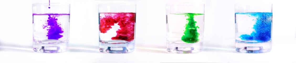On a white background four glass transparent glasses with water, in each drip multicolored paints. Ink blurs in the water, form beautiful patterns.