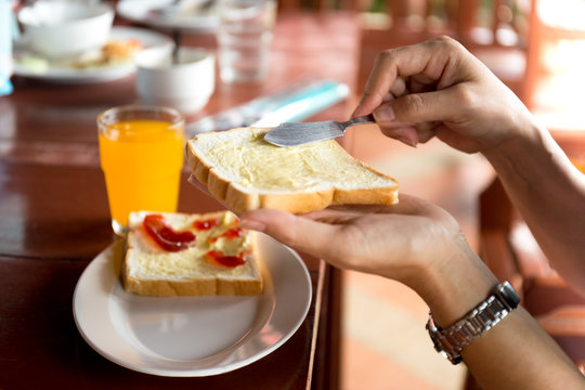 Breakfast with woman hand spreads butter on slice of bread and orange juice