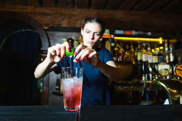 The bartender girl creates a nice cool red cocktail at the bar. The barman squeezes lime juice into an alcoholic cocktail.