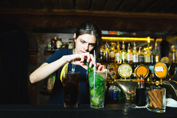 A woman bartender creates a nice alcoholic cocktail at the bar. The barman decorates mint cocktails. Bright alcoholic beverage.