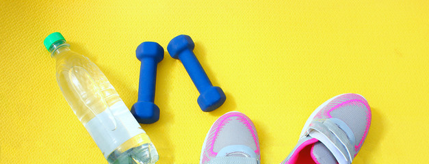 Rug yellow with dumbbells, a bottle of water and sneakers on the fresh green grass in the open air