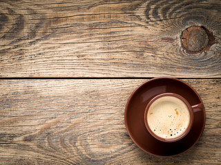 black frothy coffee with foam in brown cup with plate on aged wooden background